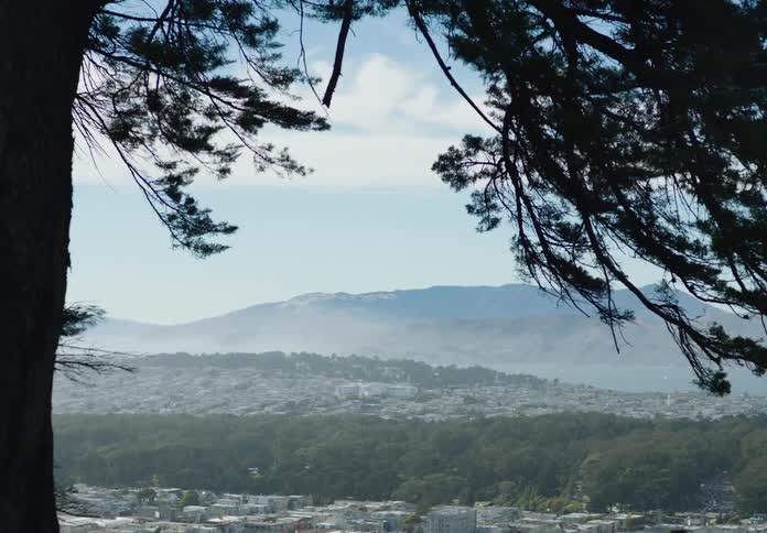 A city sits in a valley surrounded by forests with a mountain range in the distance