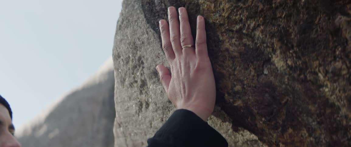 An adult is running a hand down a large rock face