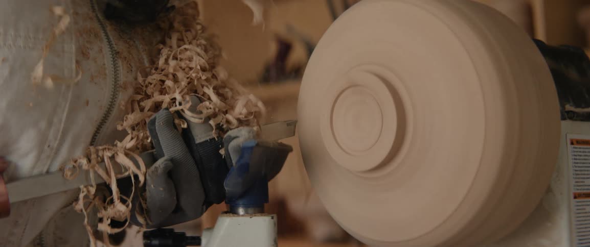 A carpenter uses a hand tool and a machine to carve a piece of wood