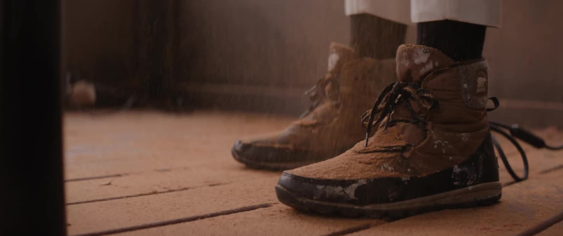Feet wearing lace up ankle boots stand on wood plank floor as sawdust falls