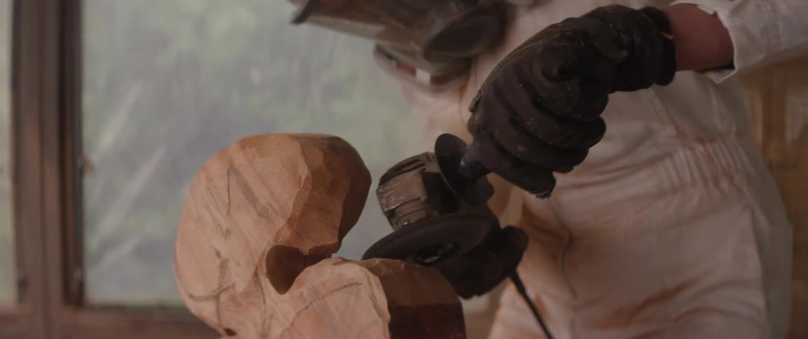 A sculptor finishing a piece of wood with a sander