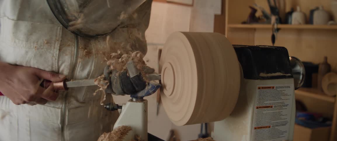 A female sculptor filing wood on a lathe