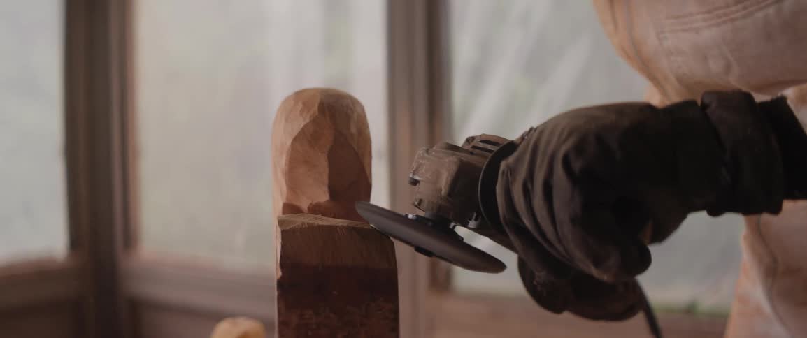 A person is using a rotary sander to sculpt a block of wood
