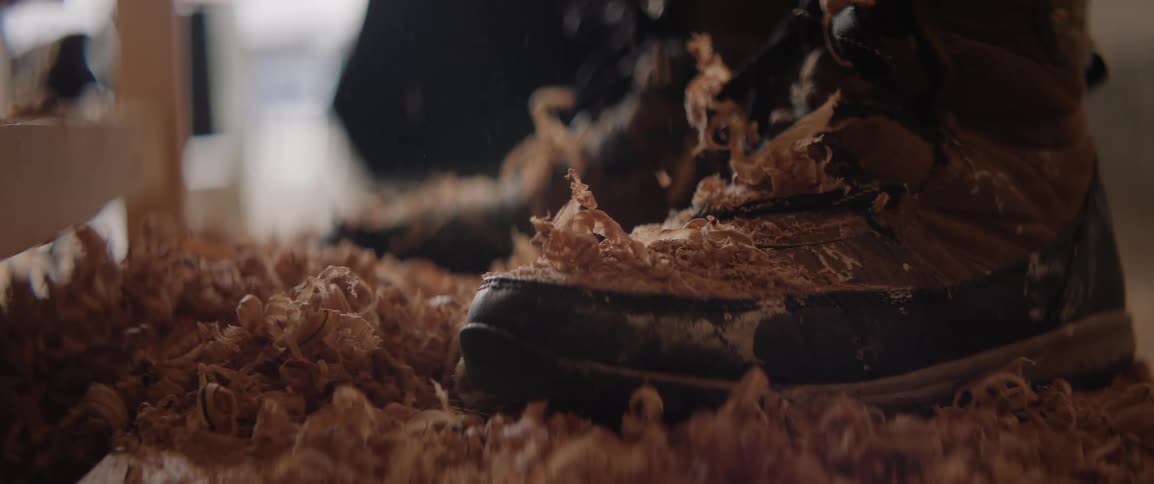 Closeup of a persons foot wearing a boot while wood shavings are falling