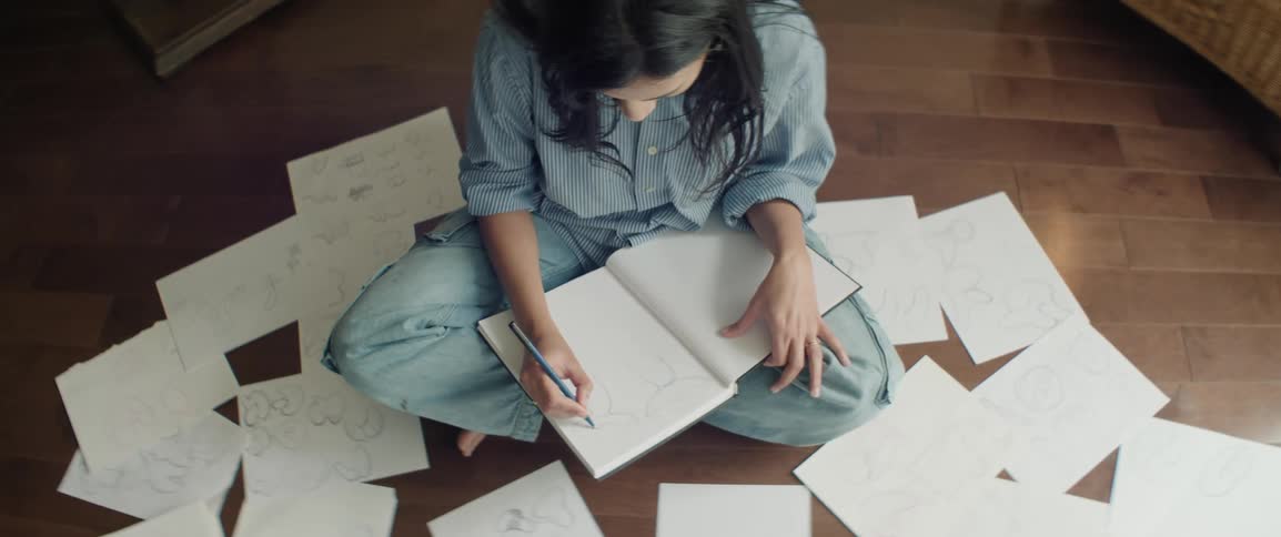 Woman sitting and drawing with papers scattered around her