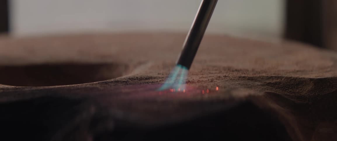 A propane torch chars the surface of a wooden sculpture