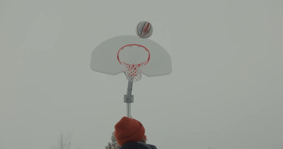Person wearing orange beanie throws basketball towards hoop and misses