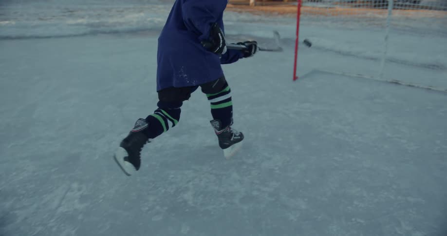 Hockey player drives hockey puck into goal while playing on outdoor ice rink near large houses during winter