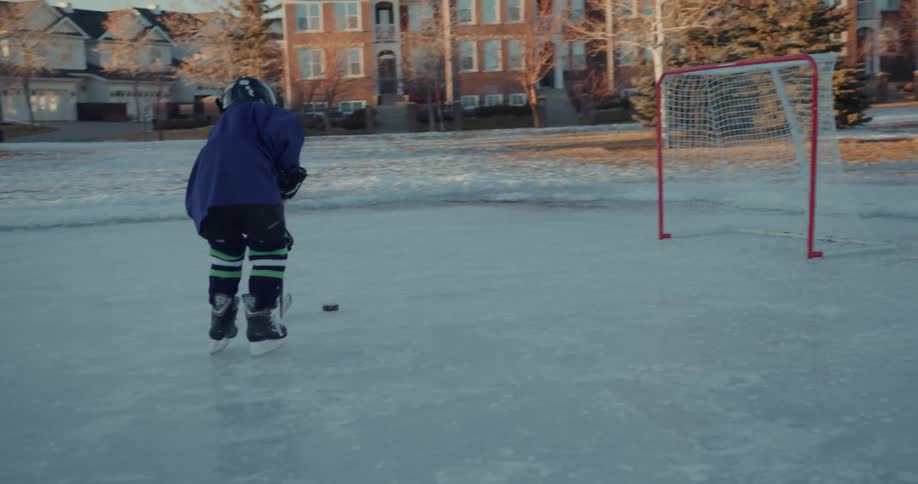 A child hockey player skating on ice hits a puck into a goal