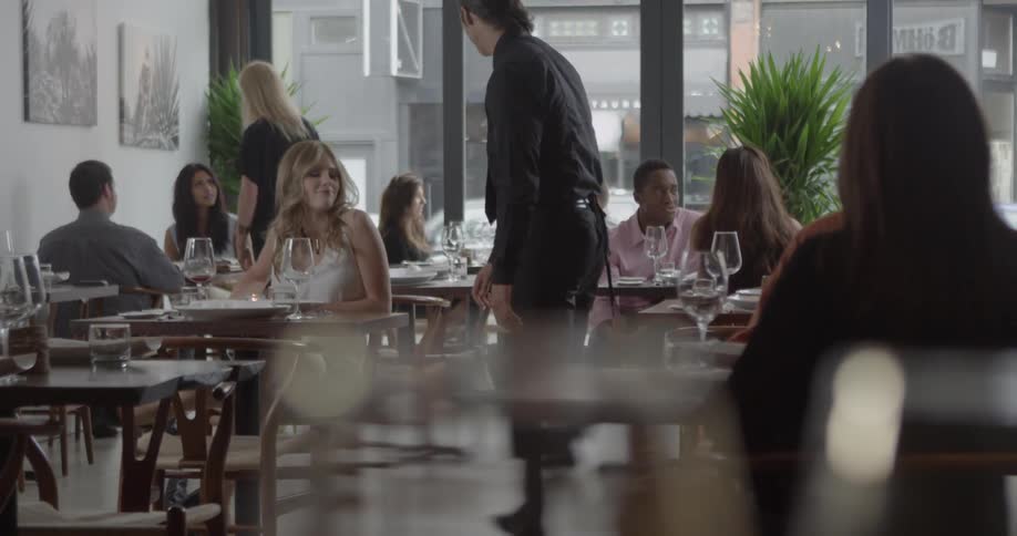 A waiter seats a woman at a table in a restaurant