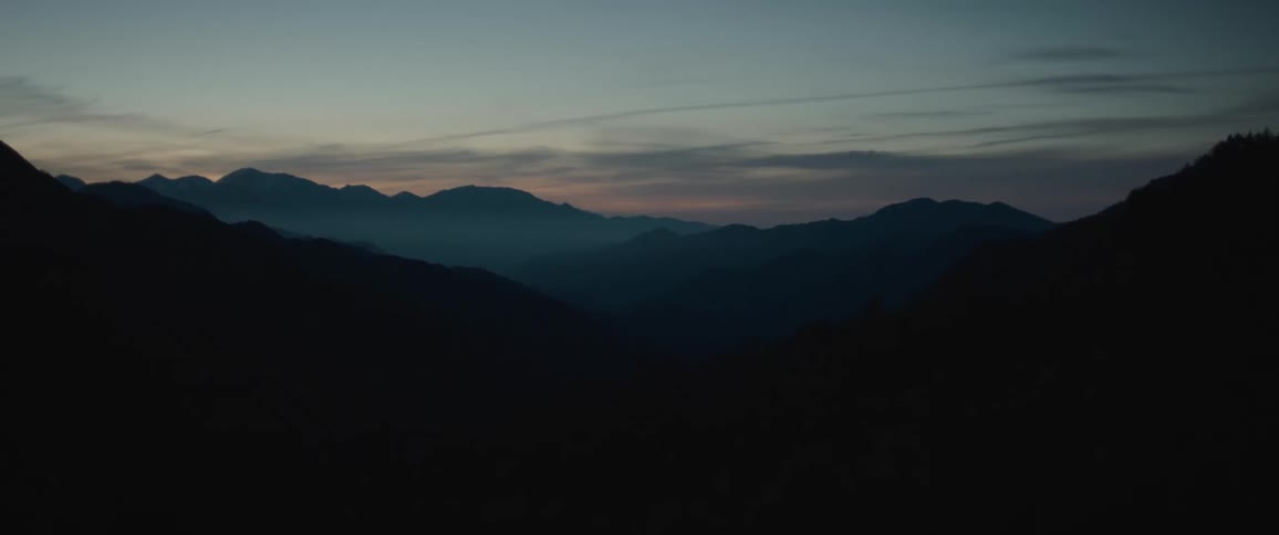 Mountain landscape silhouette with a foggy partially lit sky from below the horizon in the background