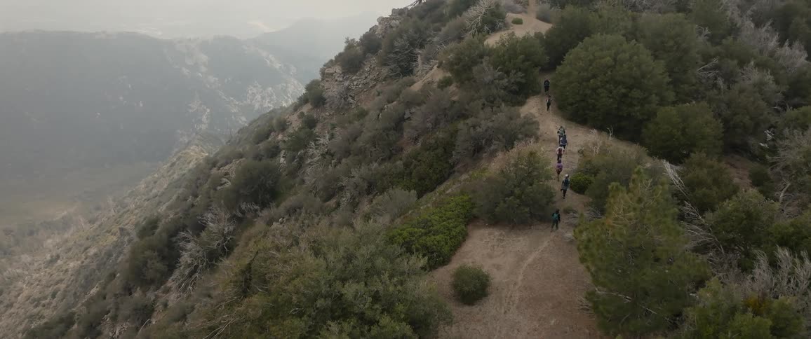 Aerial view of a trail along a mountain ridge surrounded by vegetation with backpackers on a cloudy day