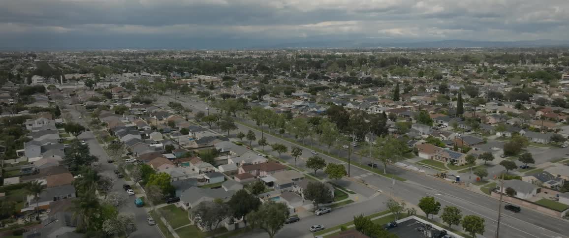 Cars pass through suburbs on divided road on an overcast day