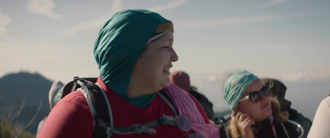 One of a group of female hikers points toward mountains as others smile and talk with her