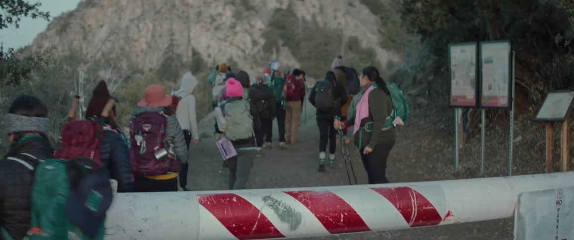 A group of young woman backpackers walk onto a trial through the mountains past a barricade