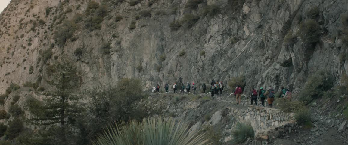 A group of hikers walk through a narrow mountain trail
