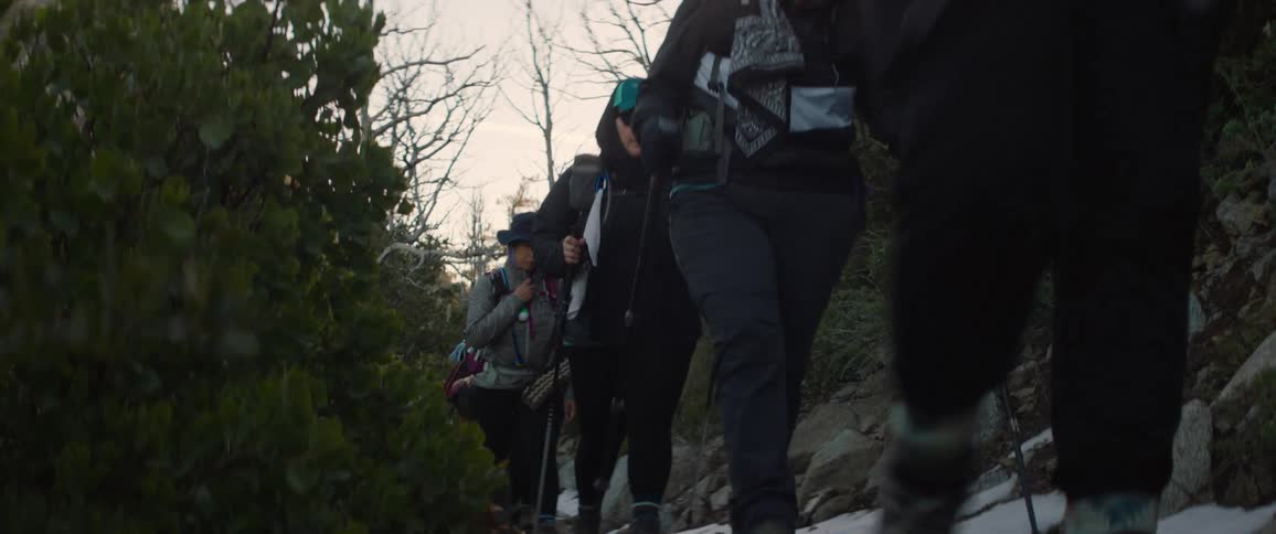 View of women walking in a line on a trail beneath a mountain