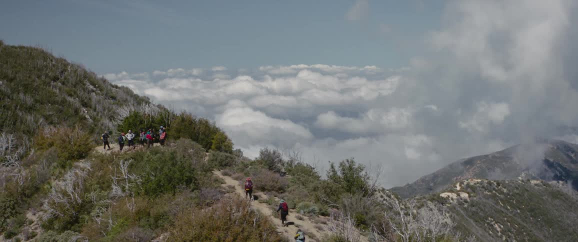 A group of hikers walking a path across the woods and up a mountain stopping on a plateau
