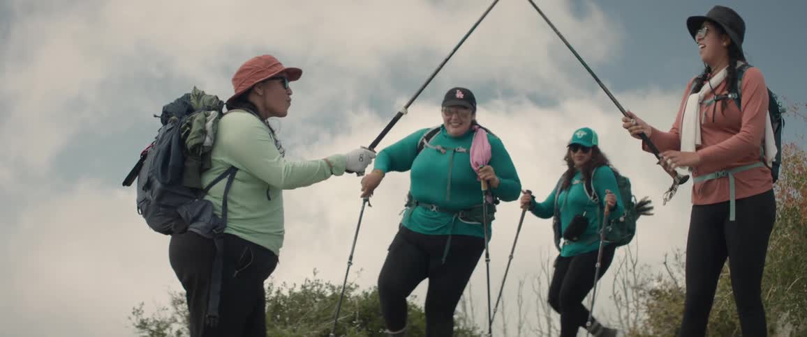 Two hikers make a pretend archway with their walking sticks for the others to pass under