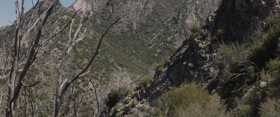 Backpackers hike along trail on mountain side on sunny day