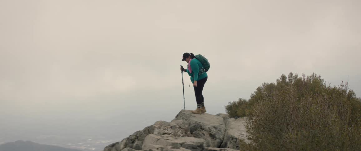 Hiker woman walking on top of a rock on a cliff beneath a mountain