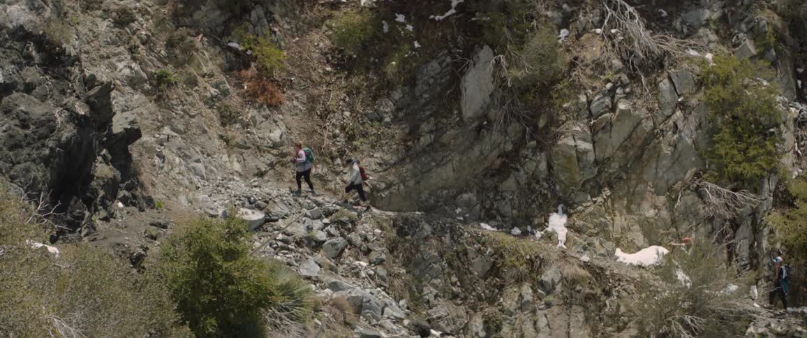 Backpackers hike along narrow trail on mountain side