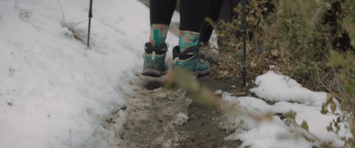 Hikers walk along narrow trail over muddy snow during a winter day