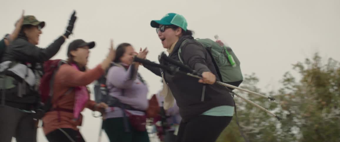 Women running and clapping hands with other women all equipped with trail clothes and backpacks