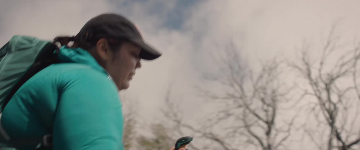 An overweight woman uses poles to help herself while hiking uphill