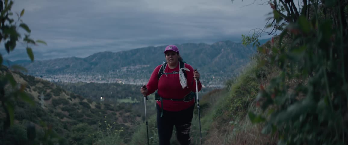 Woman wearing cap backpack and trekking pole hikes up landscape