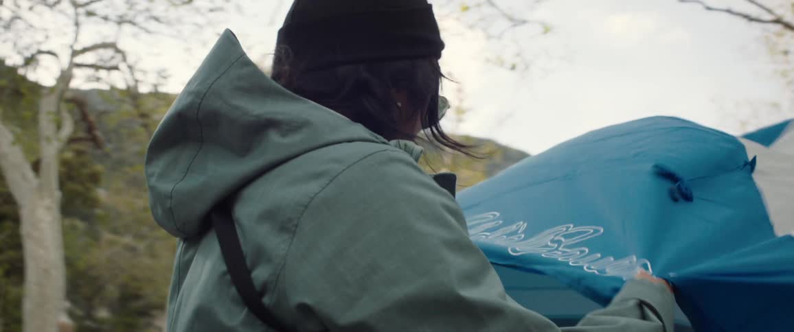 Woman holding the edge of a tent and setting it up in a forest in daylight