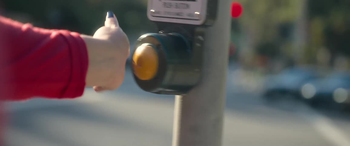 Female pedestrian presses button to activate pedestrian walk signal at intersection