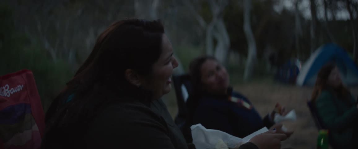 Friends sitting in chairs in the midst of a camping at night eating