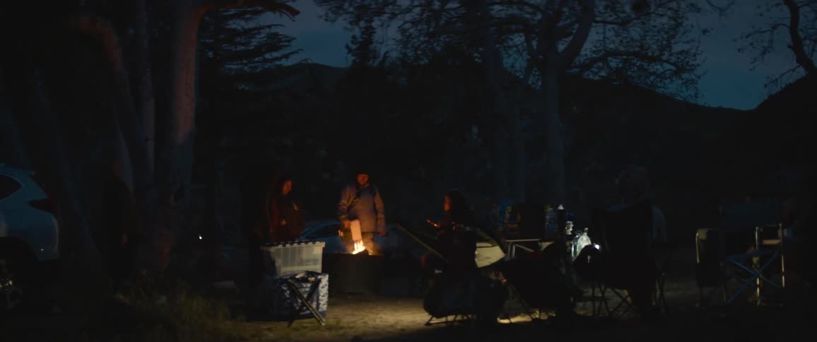 Person stands fanning fire at campsite at night