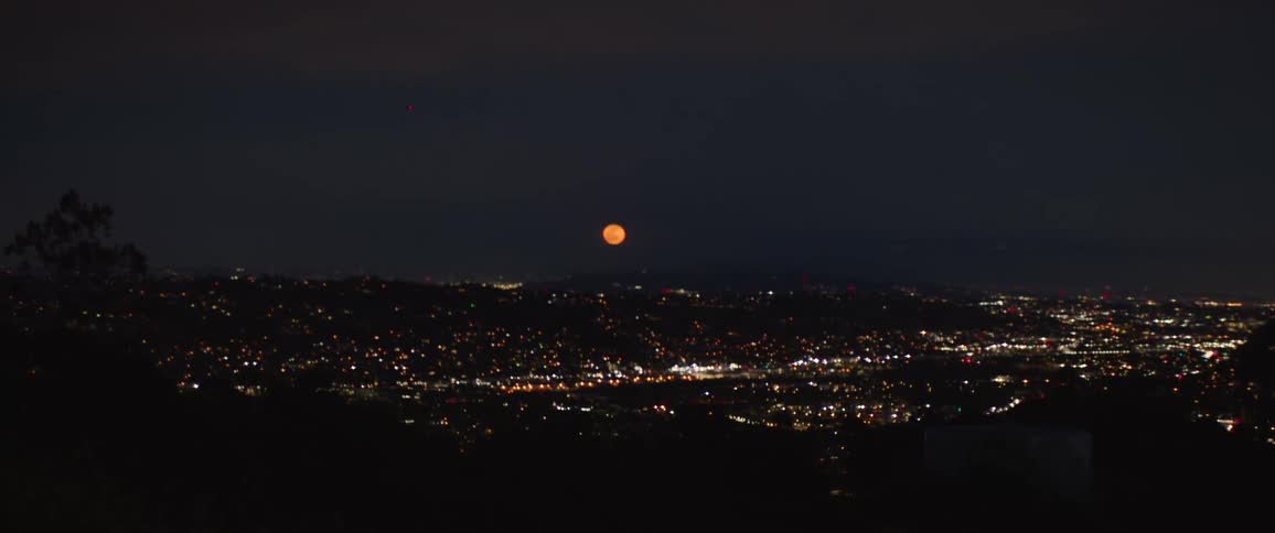 Panoramic view of a city at night with the full moon on the horizon