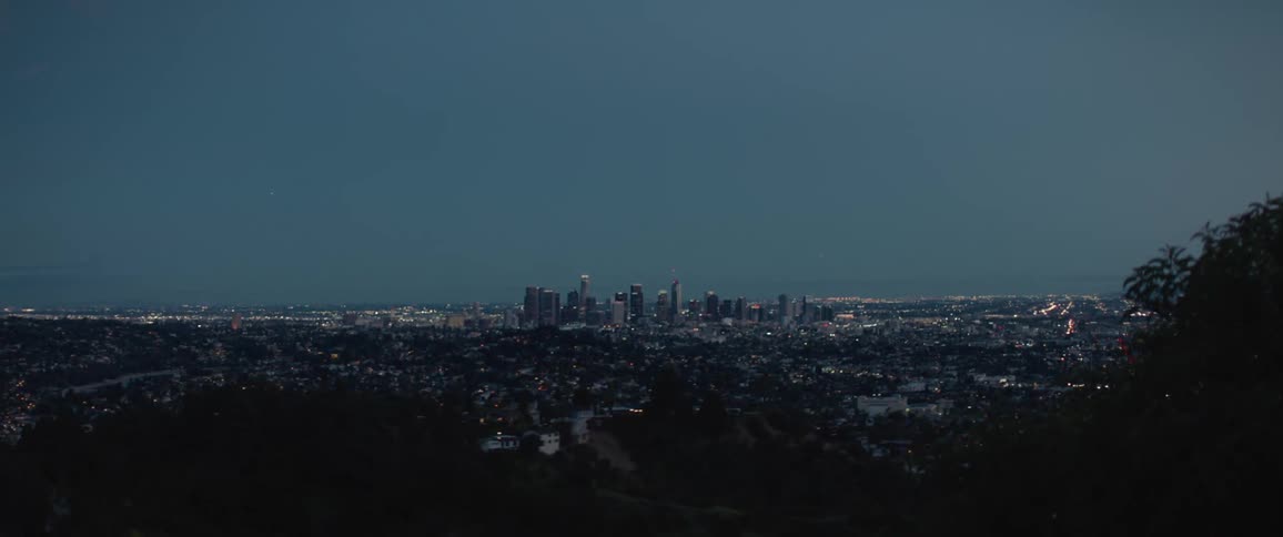 Buildings on mountain overlook city scape centered around skyline after dusk