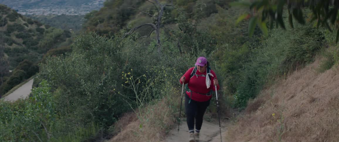 Female backpacker walks along trail on mountain slope over road