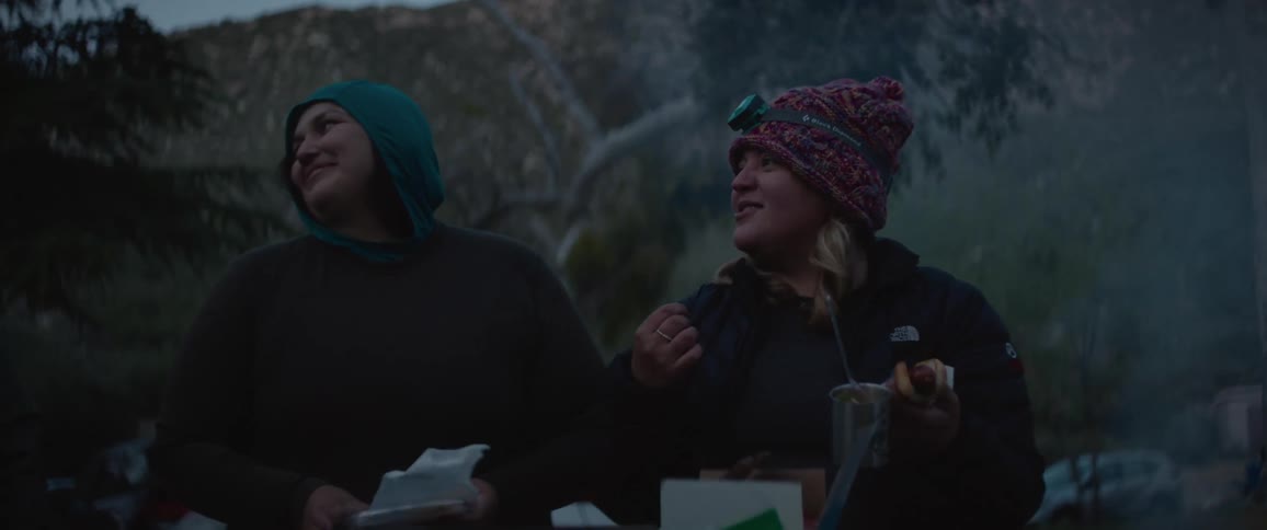 Two friends with food in their hands smiling and talking in the midst of a forest