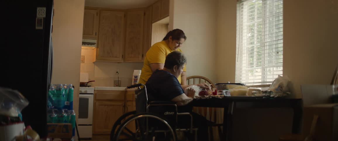 Two women one standing and another on a wheelchair take food out of plastic bags and put it on the table