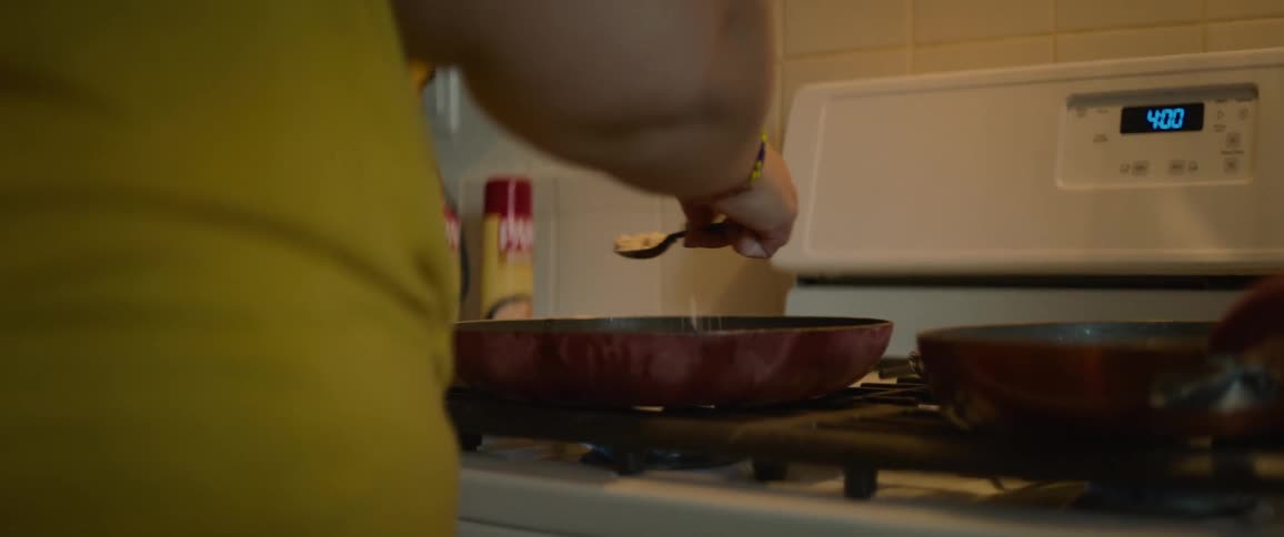 An adult is sprinkling spices in a frying pan while cooking on the stove