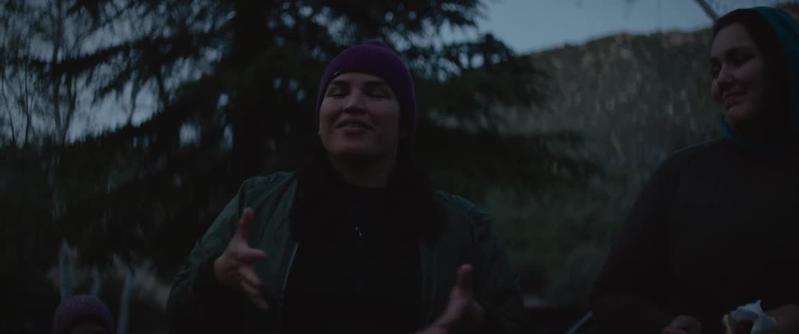 Woman animatedly talking with her hands with others by mountains outdoors in the evening after sundown before dark