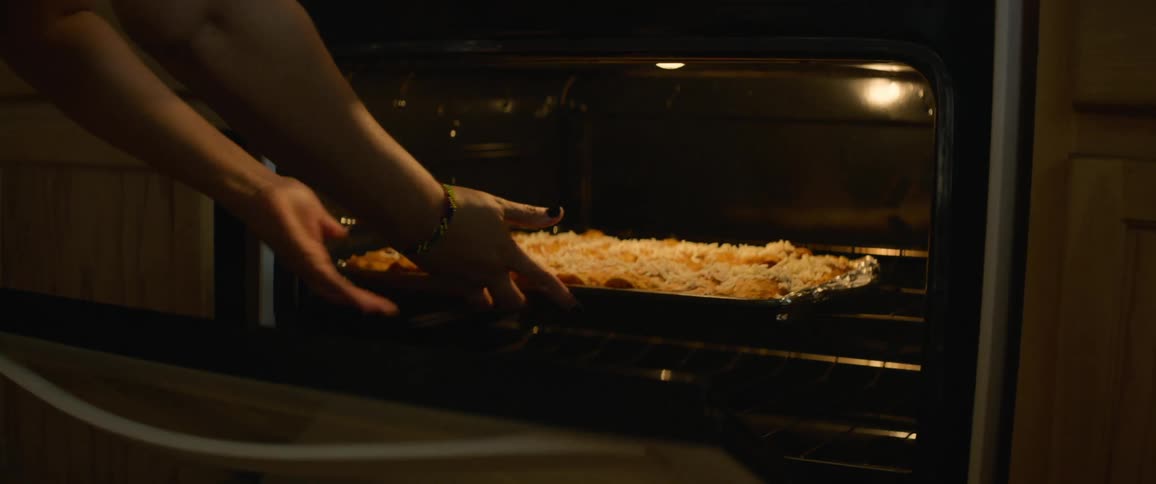 Closeup of a womans hands putting food in the oven to bake