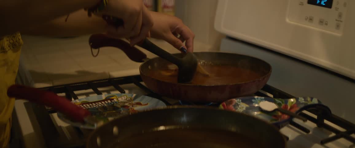 Woman tries to pick up corn tortilla she is stirring in sauce in skillet