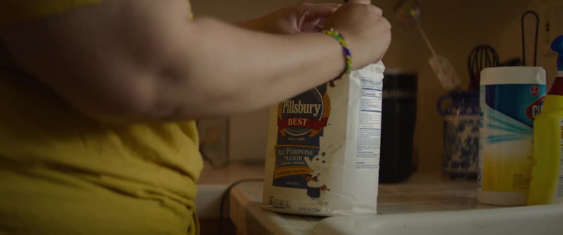 Woman opens bag of flour while standing in kitchen near sink