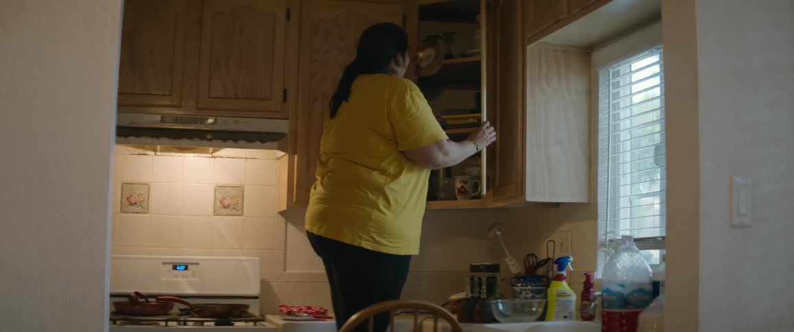 Woman standing on a chair reaching for jars in the upper kitchen cabinet
