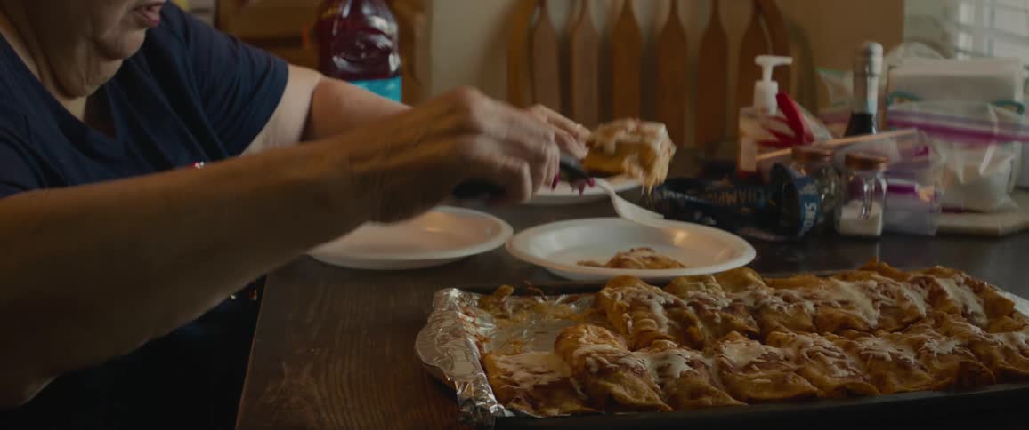 Older woman plates enchiladas while a second woman opens a bottle of juice