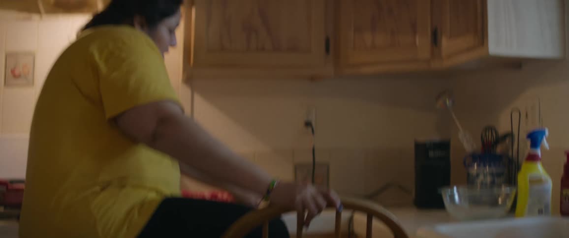 A woman climbs onto a chair to get something from the kitchen cabinet