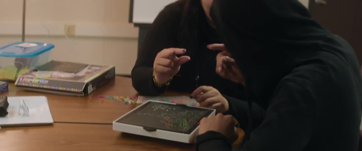 Woman smiles while helping older youth with a lite brite game board during a lesson