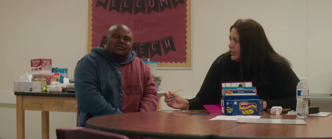 Female teacher tutors adult student using flashcards while sitting at table with snacks