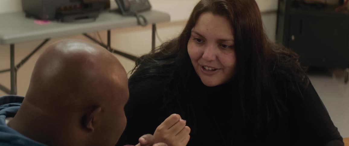 Brunette woman talks and gestures to bald black man indoors